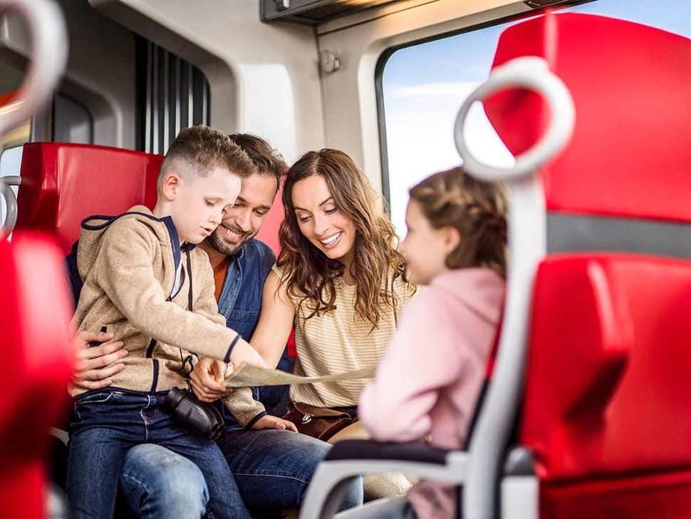 Familie mit Eltern und 2 Kinder fahren im Zug, sie lesen in einer Zeitung.
